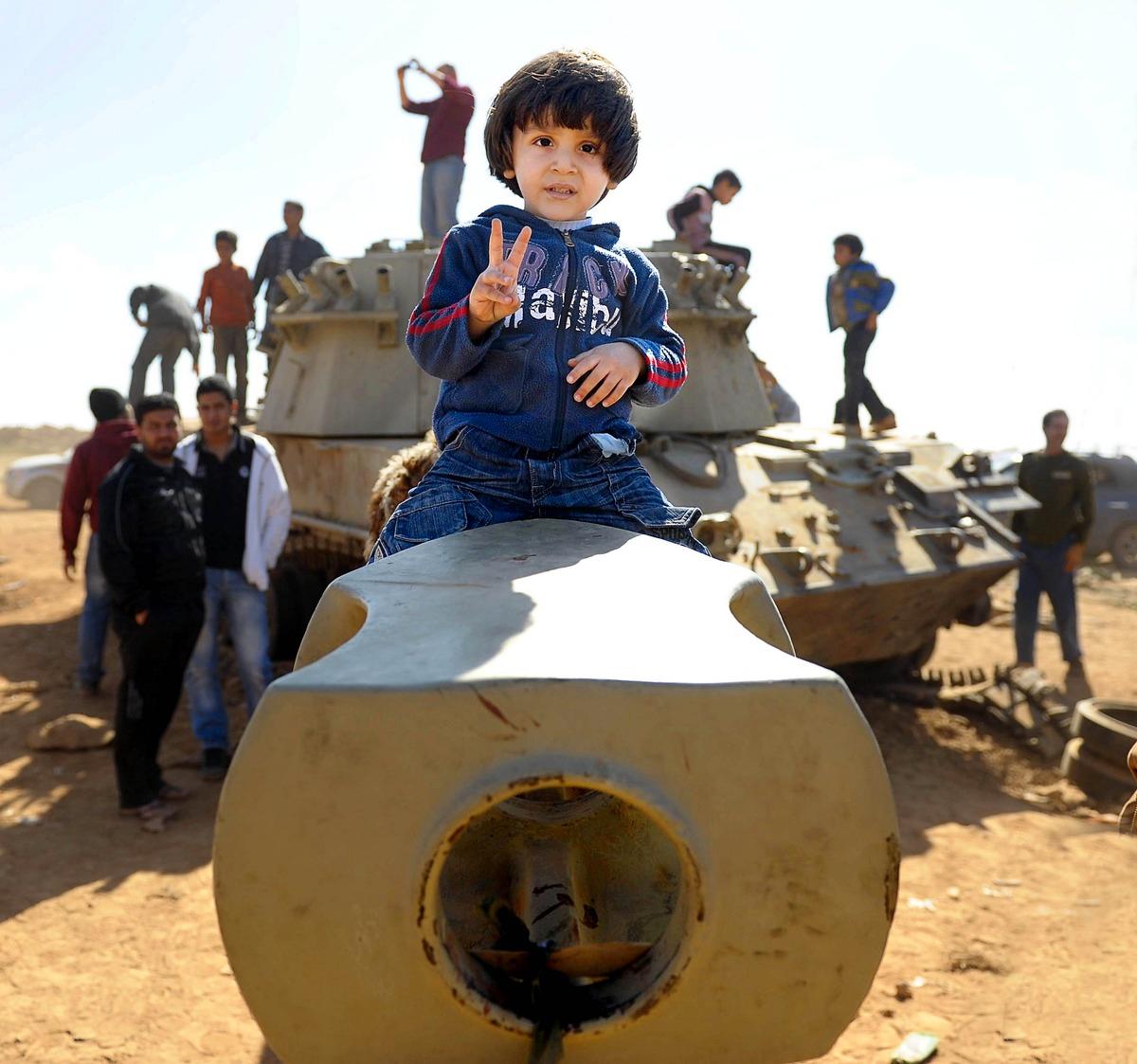 stålskelett i öknen Den lille pojken lyfts upp på kanonröret till en utbränd stridsvagn av sin pappa. Invånarna klänger på, och tar kort på, det som återstår av Gaddafis östliga pansardivision efter det franska flyganfallet. |