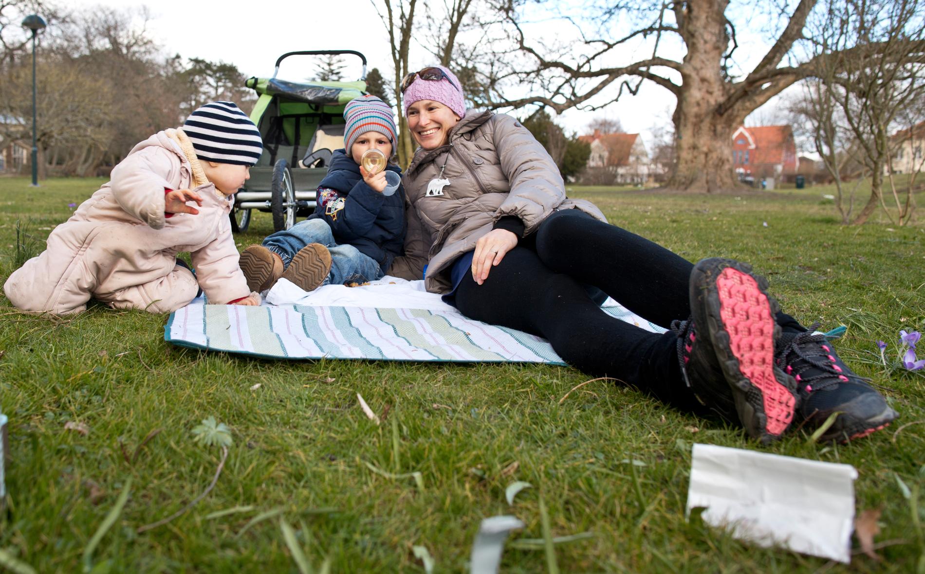 Katja Sonnenschein med sina två barn. Folk som njuter av solen i Lunds botaniska trädgård.