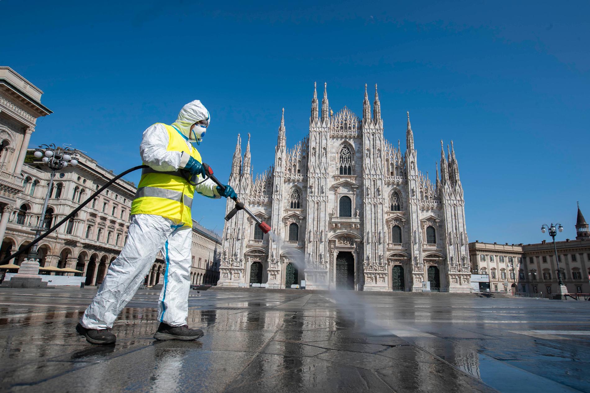 En man sprejar desinfektionsmedel på ett ödsligt Piazza del Duomo i Milano.