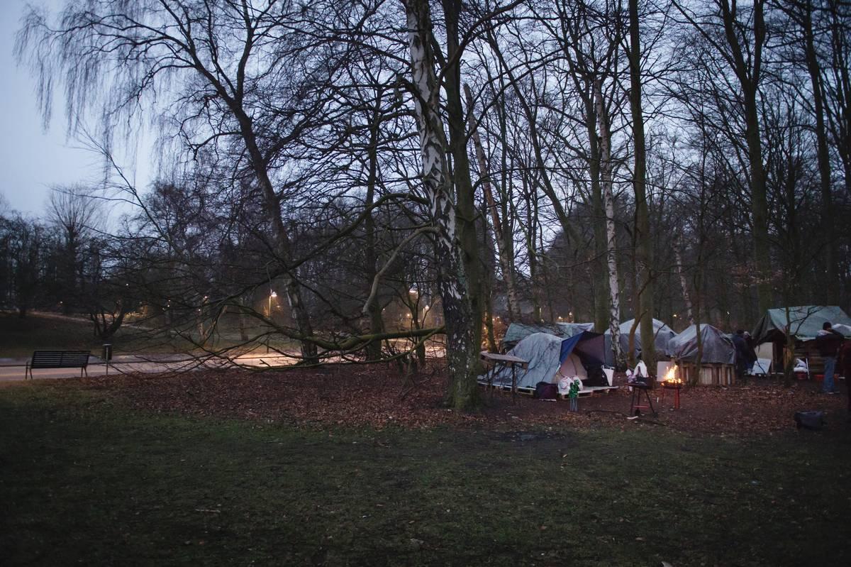 Mot kvällen drar sig EU-migranterna tillbaka till sitt läger i Pildammsparken i centrala Malmö. De värmer sig kring en brasa som snart ska användas som grill.