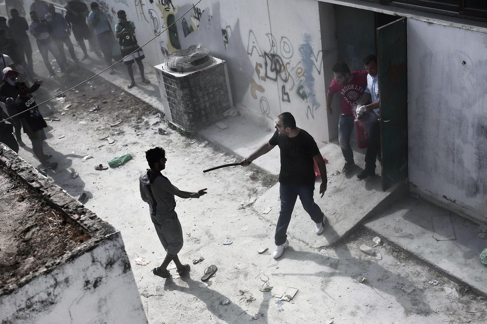 En polisman slår mot en flykting med en batong i samband med registreringen av nyanlända på fotbollsstadium på Kos, Grekland.