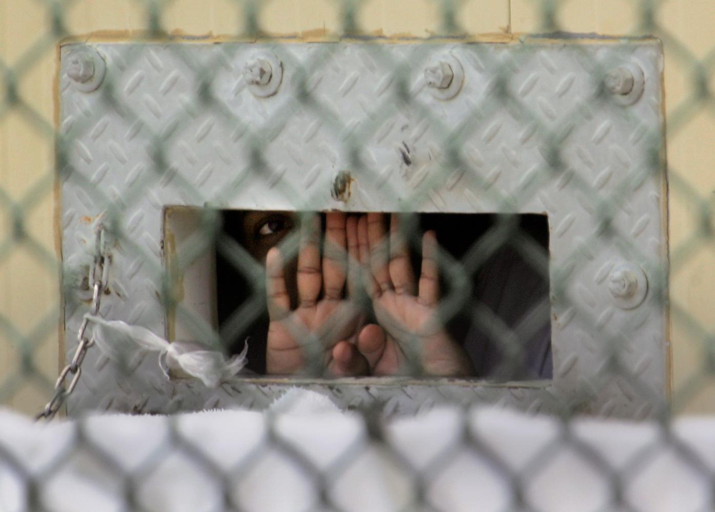 En fånge i Guantanamo kikar ut från sin cell genom ett hål i väggen.