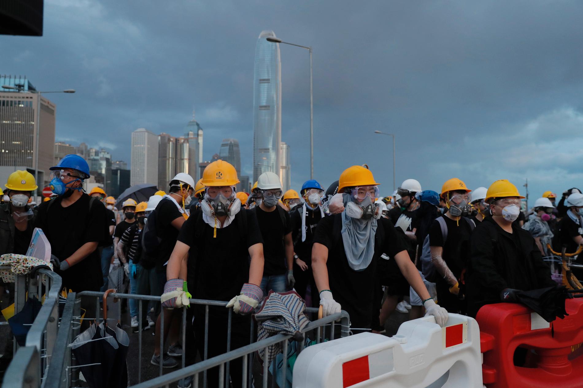 Demonstranterna, klädda i gasmasker och hjälmar, blockerar en väg under protesterna i Hongkong.