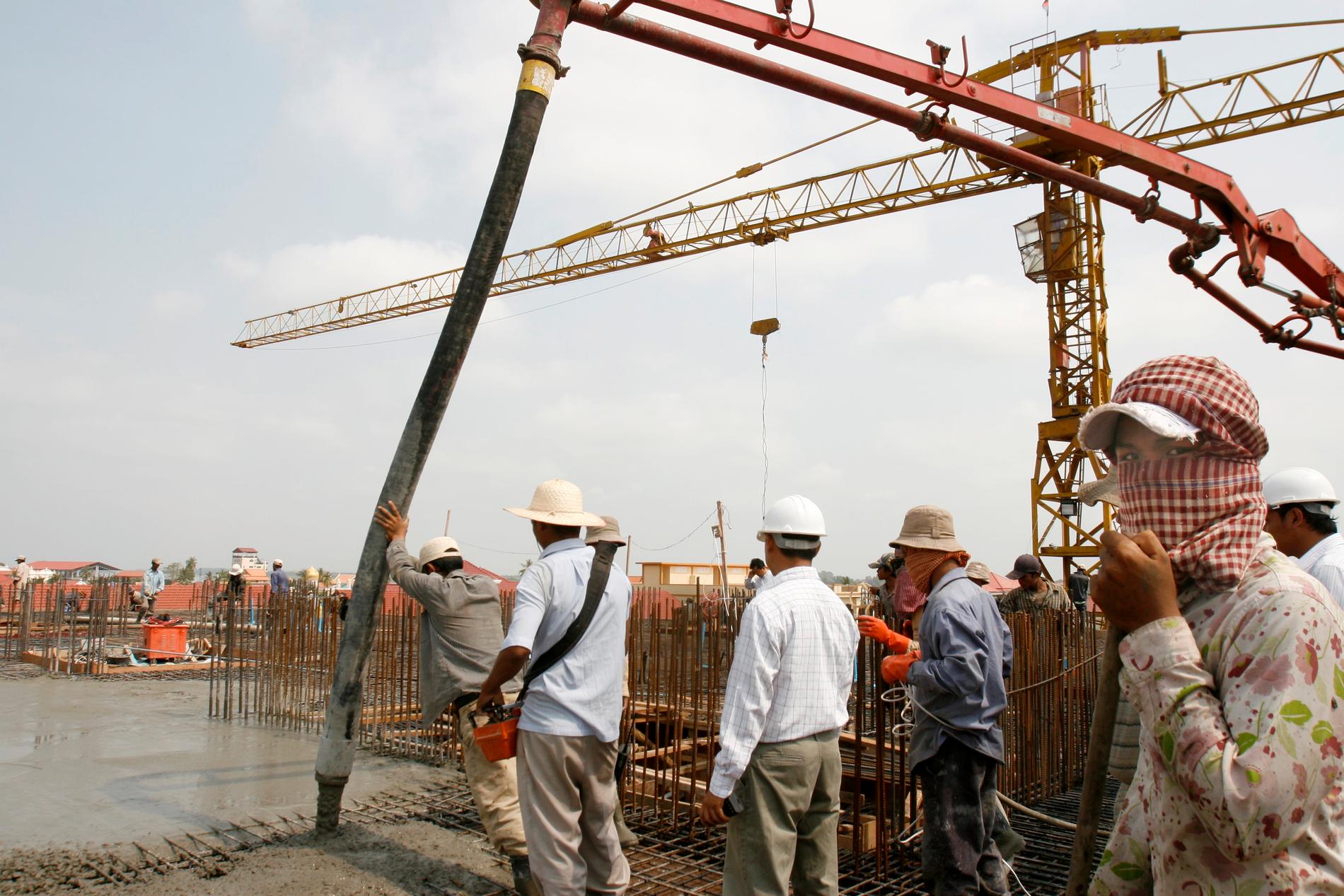 Byggnadsarbetare ser på medan cement fyller upp ett nytt lägenhetskomplex i Phnom Penh 2008. De senaste årtiondena har land- och huspriserna i huvudstaden skjutit i höjden.