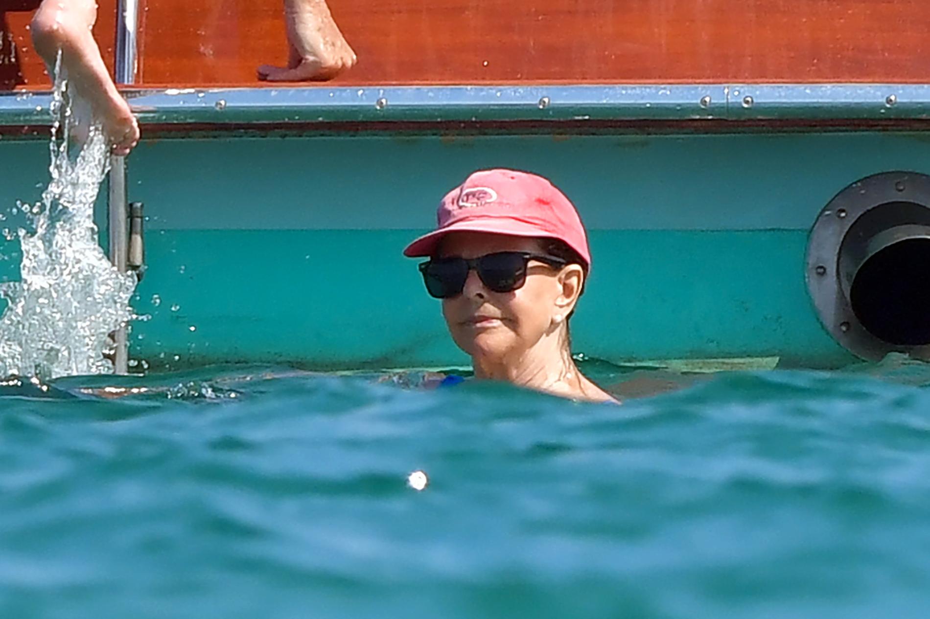 Drottningen, i keps och solglasögon, badar i havet.