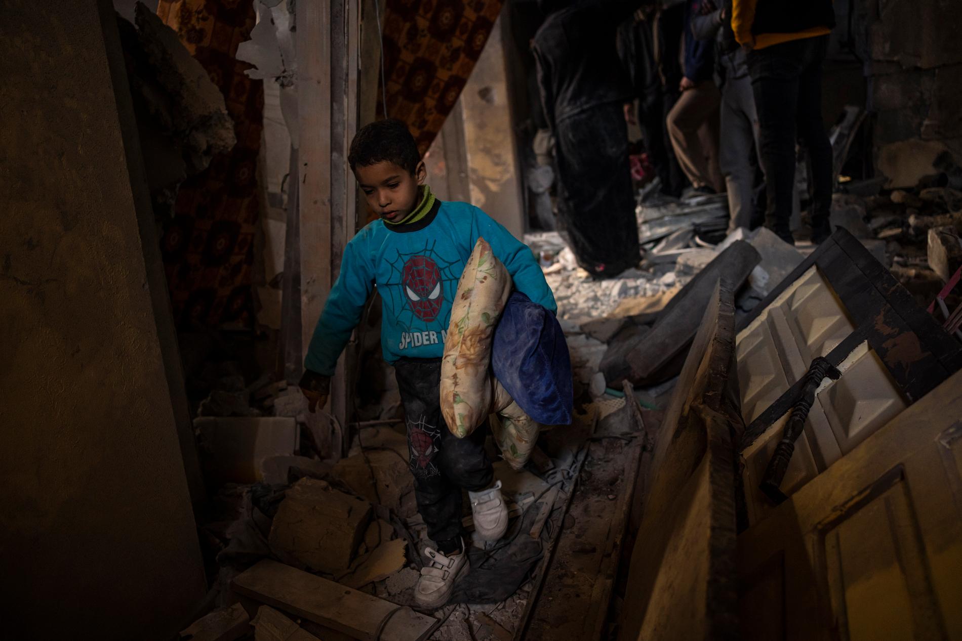En pojke samlar sina ägodelar från sitt hus som förstörts under torsdagens anfall i Rafah.