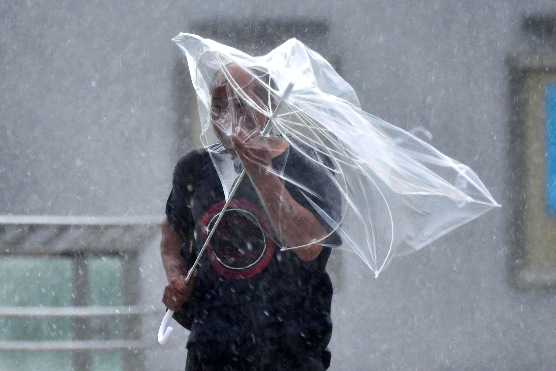 En man försöker att skydda sig mot regn och kraftiga vindar.