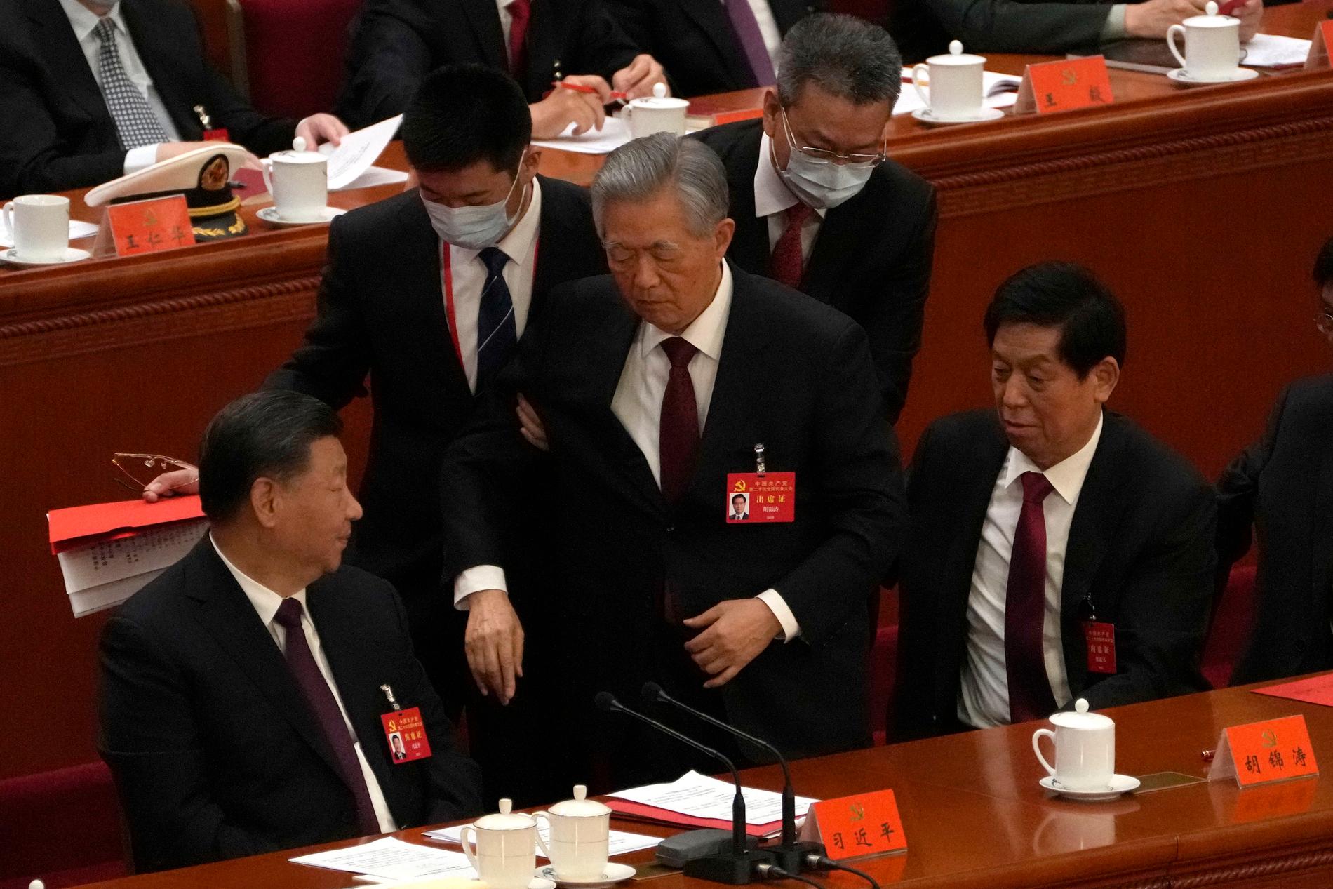 Kinas tidigare president och generalsekreterare Hu Jintao, stående i mitten, leds ut från avslutningsceremonin under Kommunistpartiets kongress.