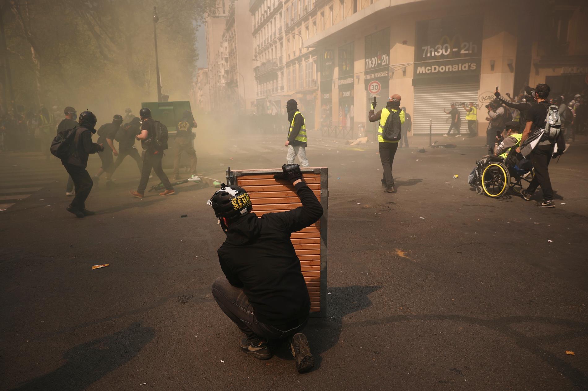 Demonstranter tar skydd bakom träpaneler vid sammandrabbningar i Paris.
