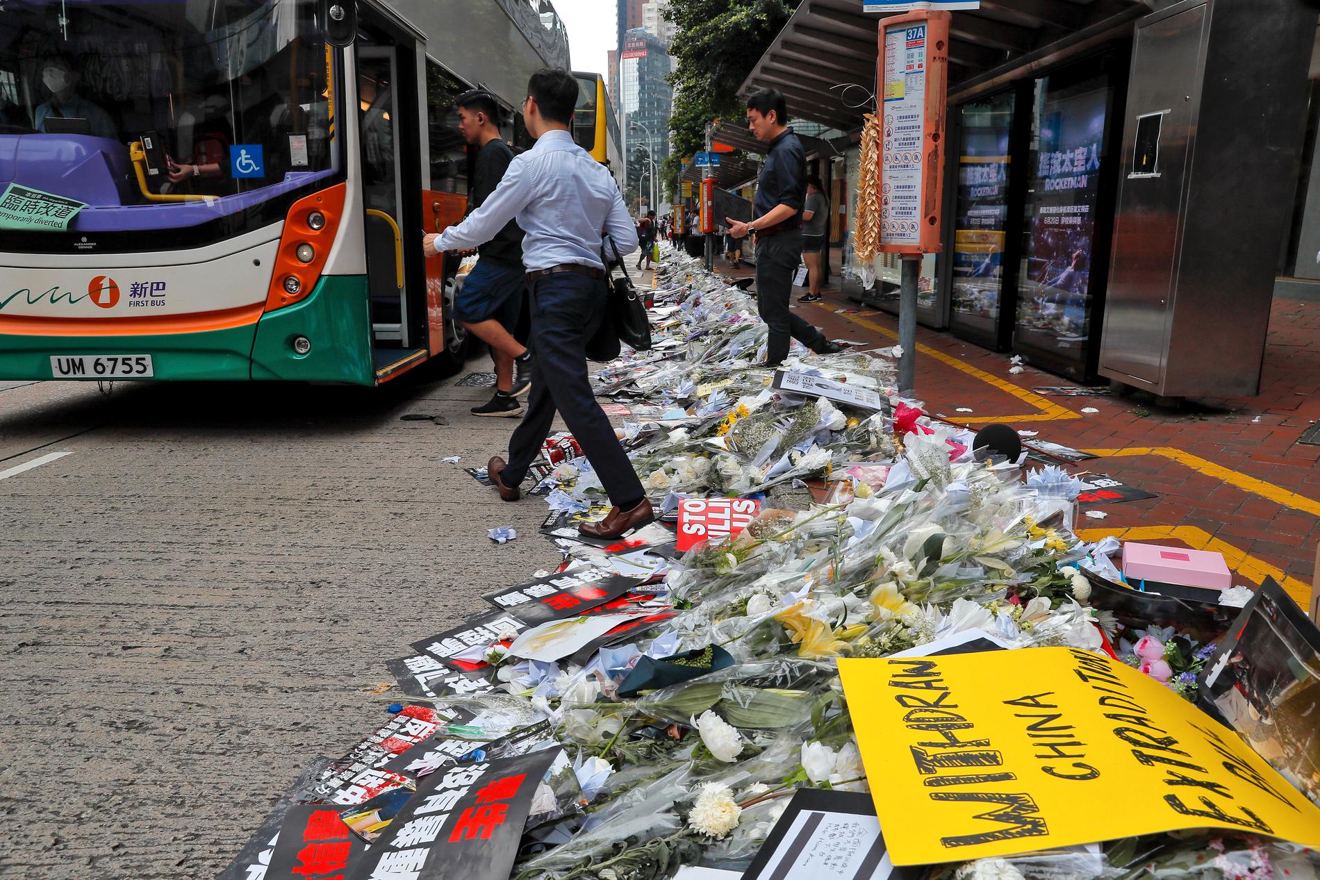Pendlare går förbi blommor och skyltar som placerats vid en busshållplats efter en av jättedemonstrationerna i Hongkong.