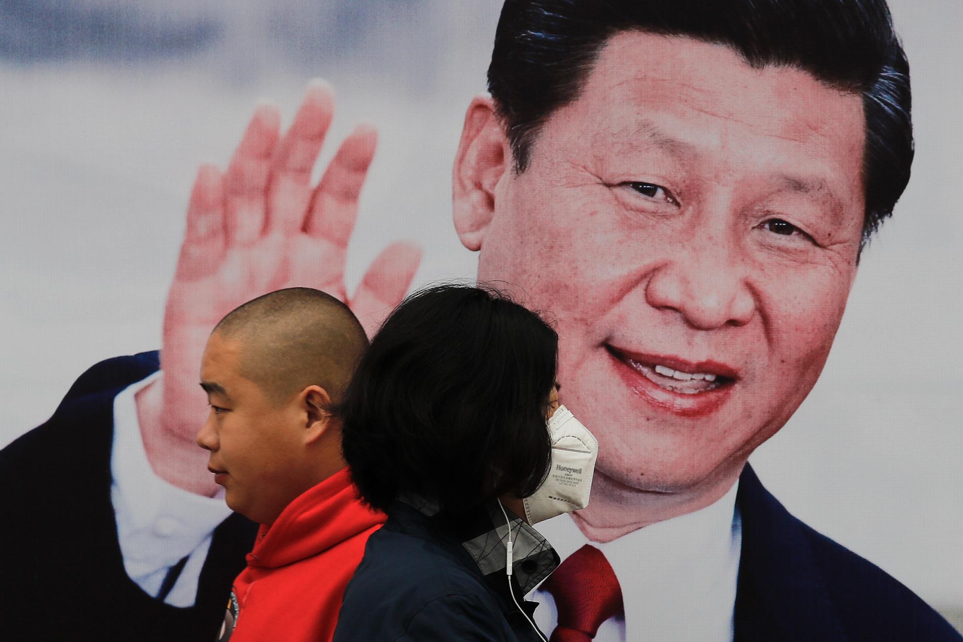 En kvinna och en man går förbi en affisch på Kinas president Xi Jinping. Arkivbild.