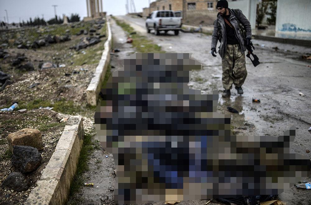 En kurdisk soldat intill en grupp ihjälskjutna IS-krigare i staden Kobane.