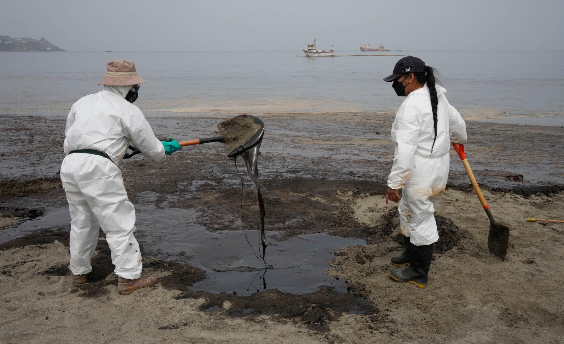 Saneringsarbetare i skyddskläder arbetar med att få bort oljan på stranden Conchitas i Ancón, Peru.