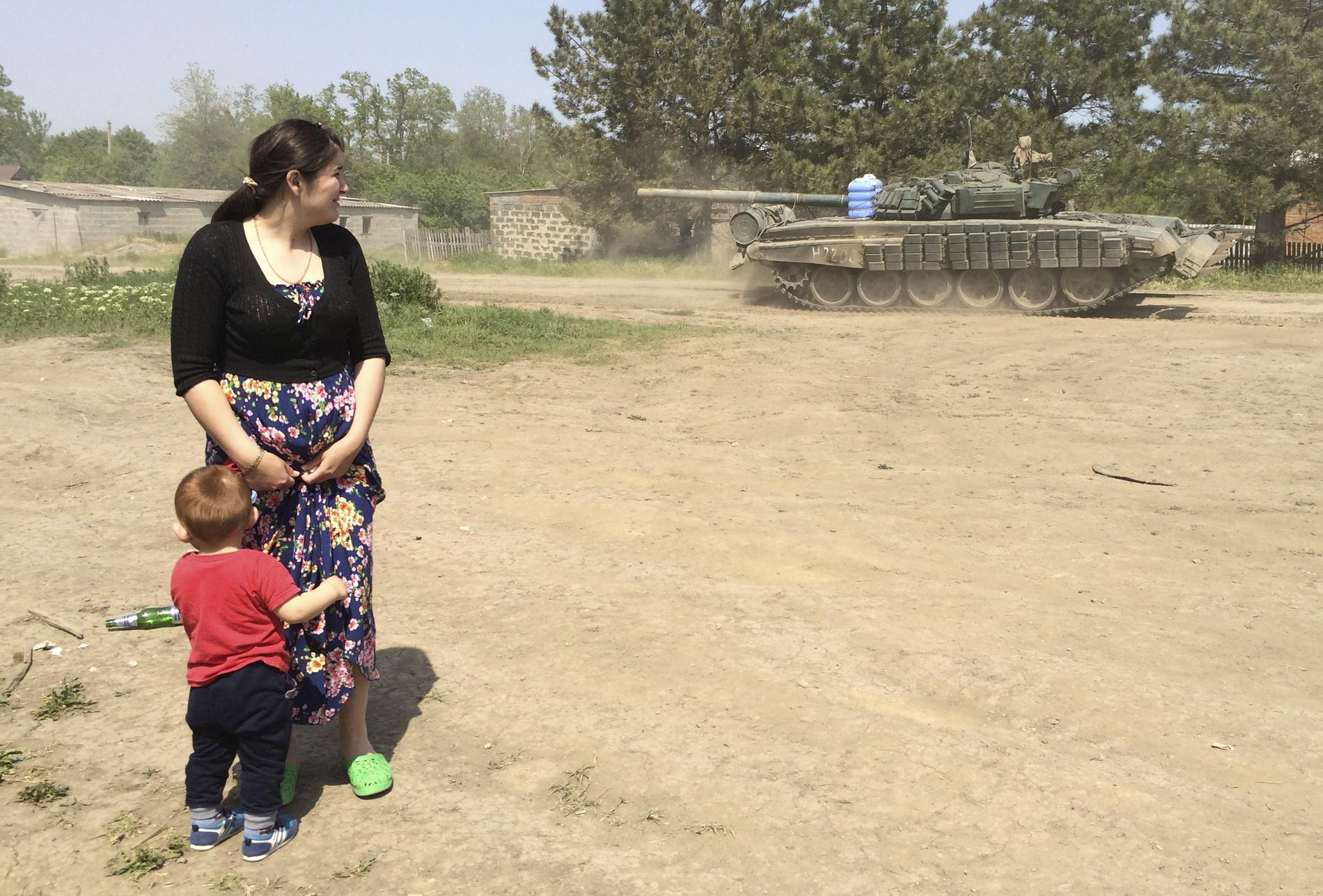 En kvinna och en pojke tittar på den ryska militärfordonen när de kör igenom Khutor Chkalova på väg mot militärbasen fem mil från den ukrainska gränsen.