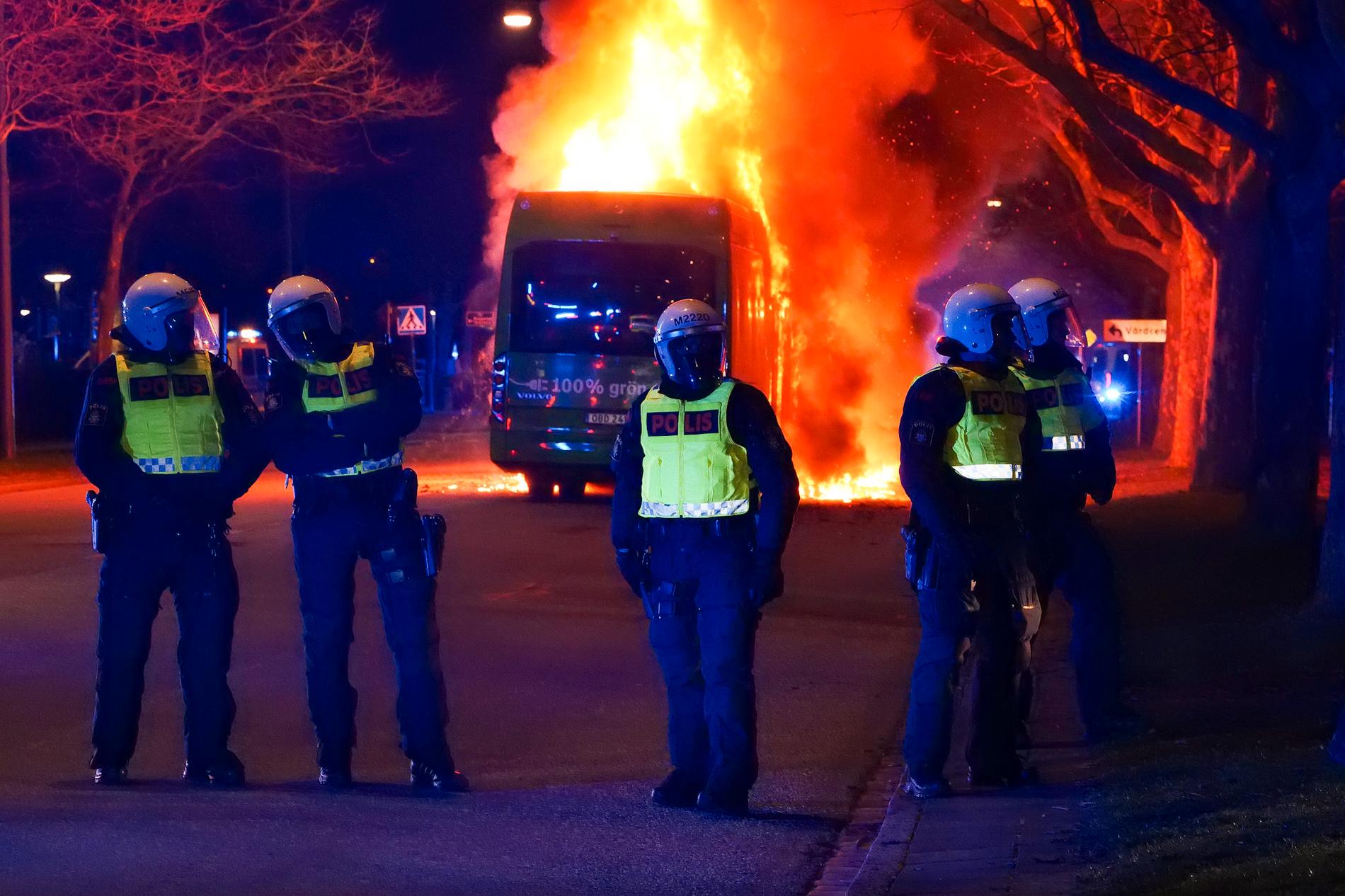 Kravallpolis framför den brinnande bussen. En stor insats med polis och räddningstjänst möts av stenkastande, enligt vittnen på platsen. 