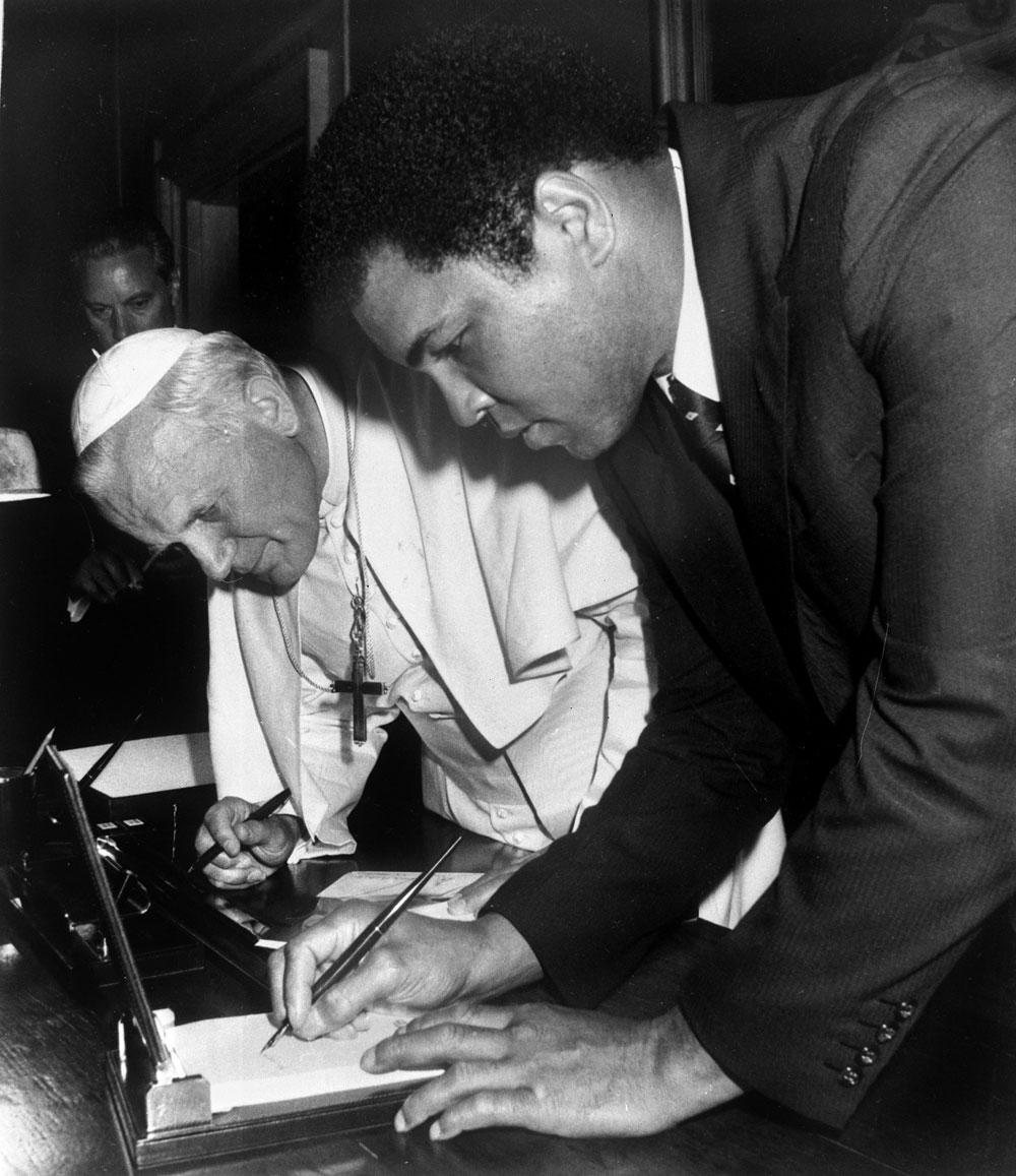 ALI OCH PÅVEN Påven John Paul II smygtittar på hur Muhammad Ali skriver sin autograf i Vatikanen 1982. Ali fick god träning på det under sin karriär.