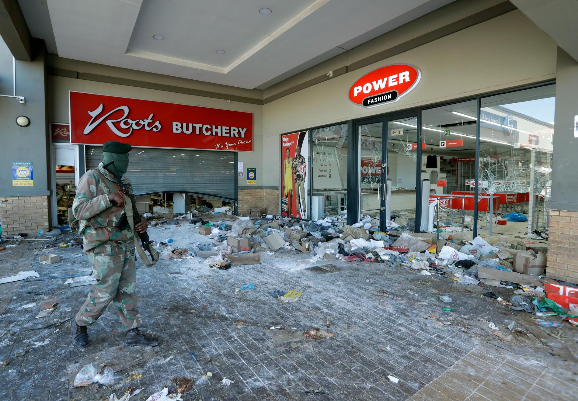 En soldat patrullerar vid ett plundrat köpcentrum i Soweto utanför Johannesburg.