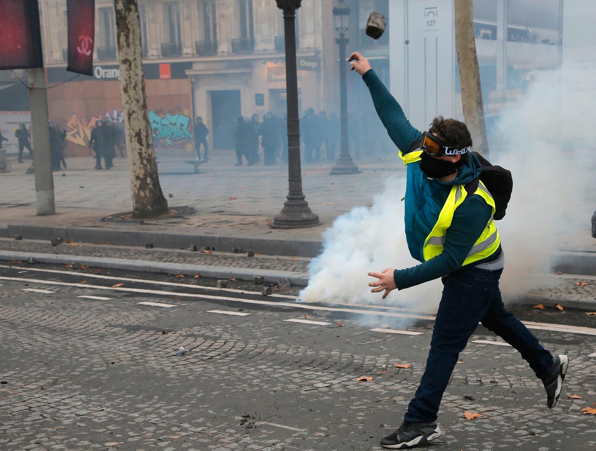 En demonstrant kastar en gatsten mot polisen på Champs-Élysées under lördagens protester i Paris.
