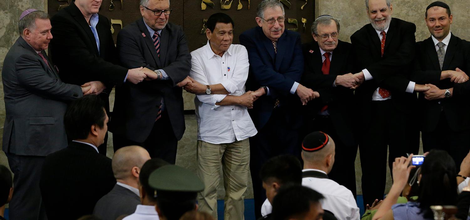Filippinernas dåvarande presidenten Rodrigo Duterte (fjärde personen från vänster) i armlänk med Israels ambassadör Effie Ben Matityau (tredje från vänster) och medlemmar av den judiska föreningen i Filippinerna under ett möte i Beit Yaacov -synagogan i Makati, söder om Manila, 2016. Duterte hade då bett judar över hela världen om ursäkt efter att han dragit en jämförelse mellan hans blodiga narkotikakrig i Filippinerna och Hitlers Förintelsen, vilket fått många judar att rasa. 