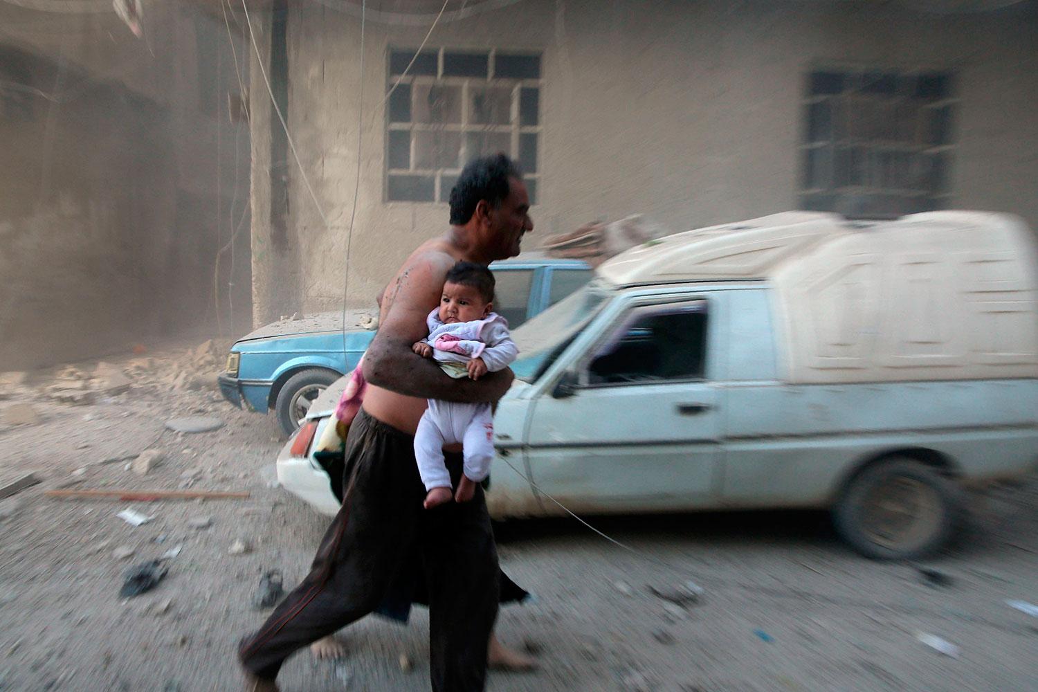 En man flyr i bara byxorna med ett litet barn under armen i Kafr Batna strax efter att bomberna slagit ner.