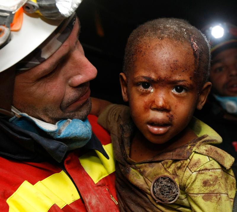 En spansk hjälparbetare bär undan tvåårige Redjeson Hausteen Claude efter att han räddats från sitt kollapsade hem. Pojken hade varit fast i 48 timmar.