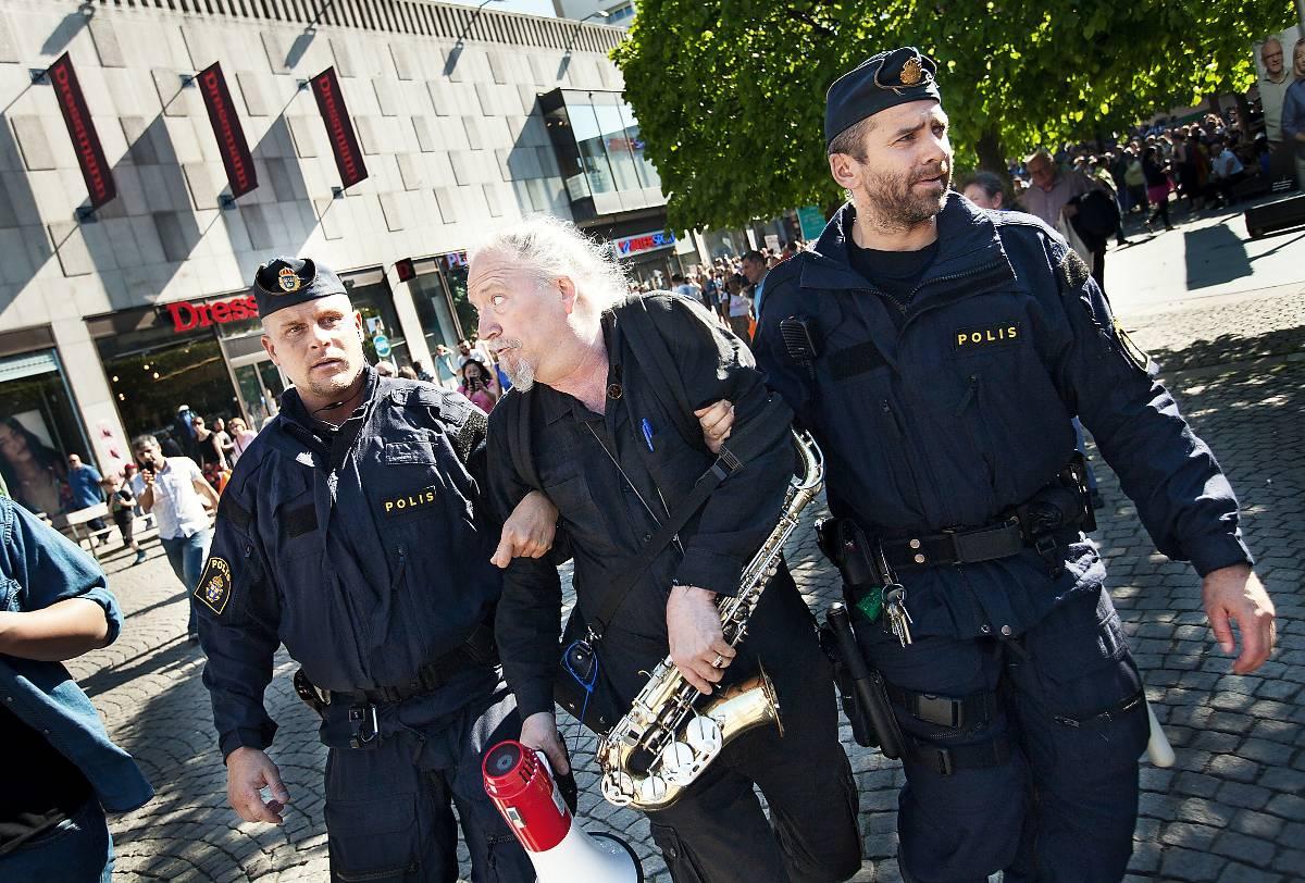 Här förs Dror Feiler (V) bort av polisen från Farsta centrum. Under ett tal av Björn Söder (SD) dök Feiler upp med sin saxofon för att protestera.