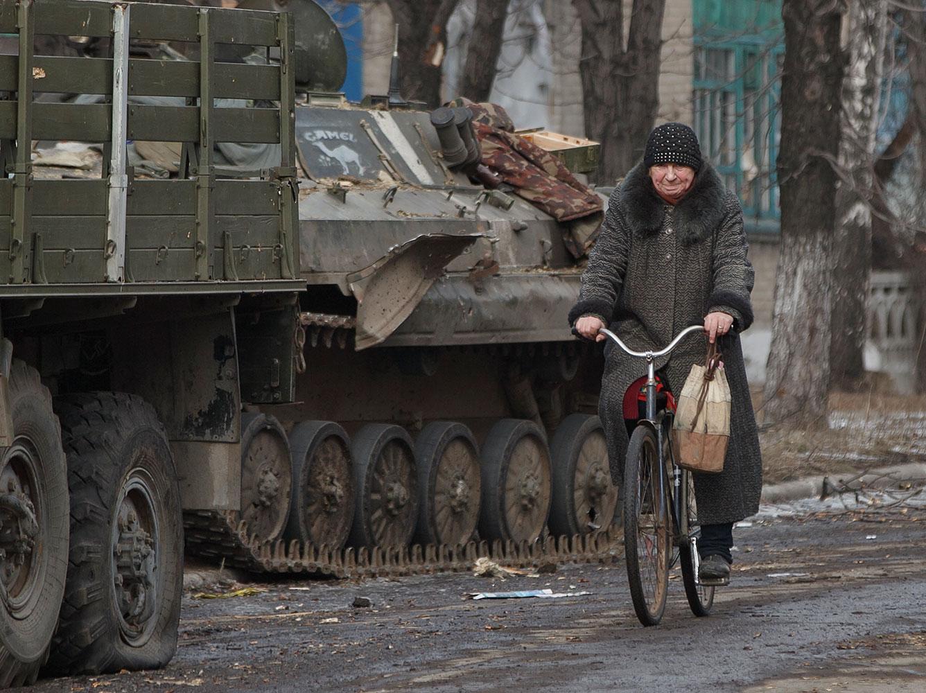 En kvinna cyklar förbi militärfordon i Debaltseve.