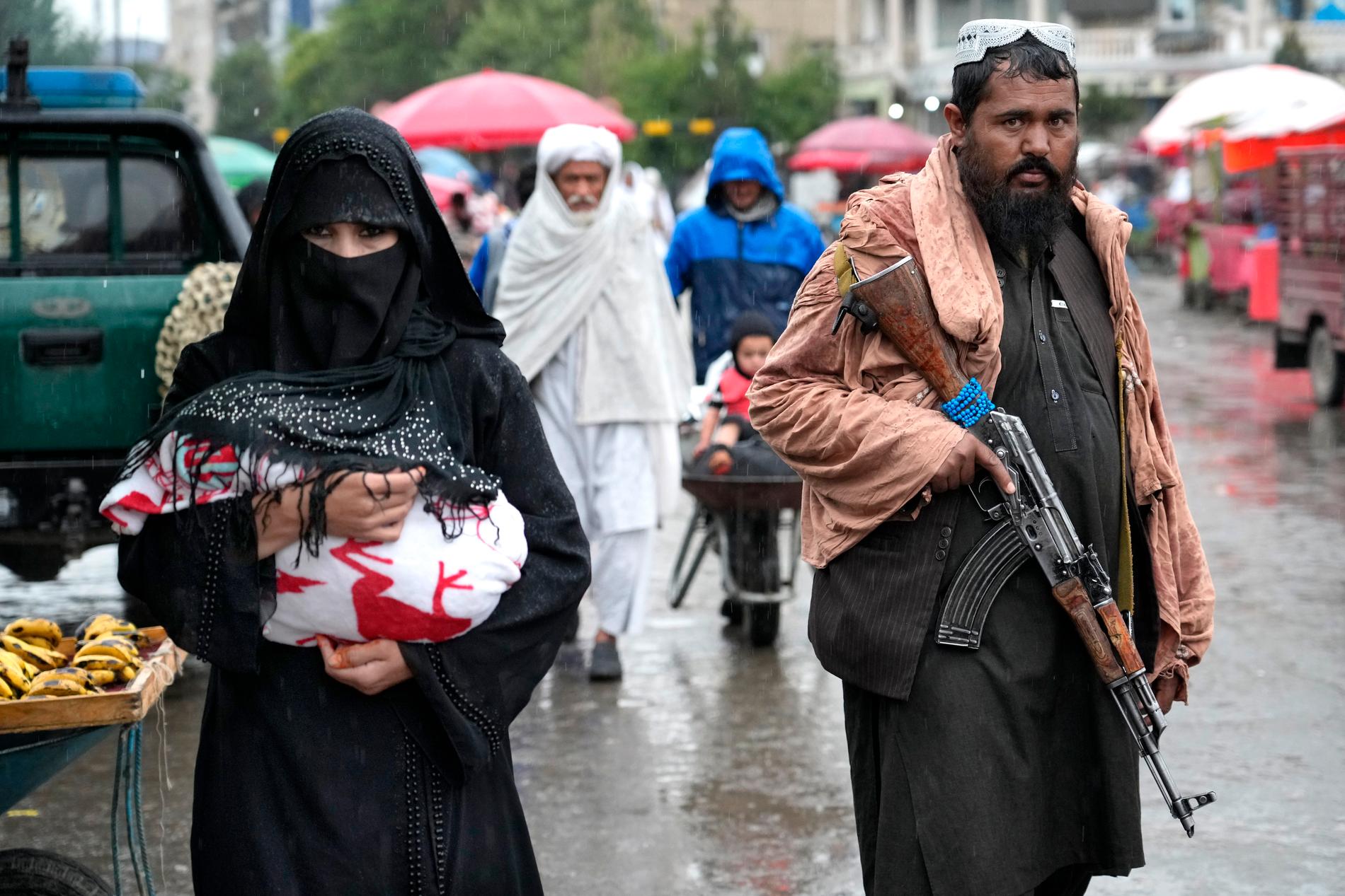 En afghansk kvinna går genom en marknad i Afghanistans huvudstad Kabul och en talibankrigare håller vakt. Arkivbild.