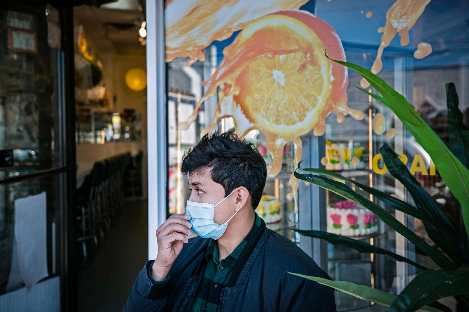 En man rättar till munskyddet utanför ett café i Corona.