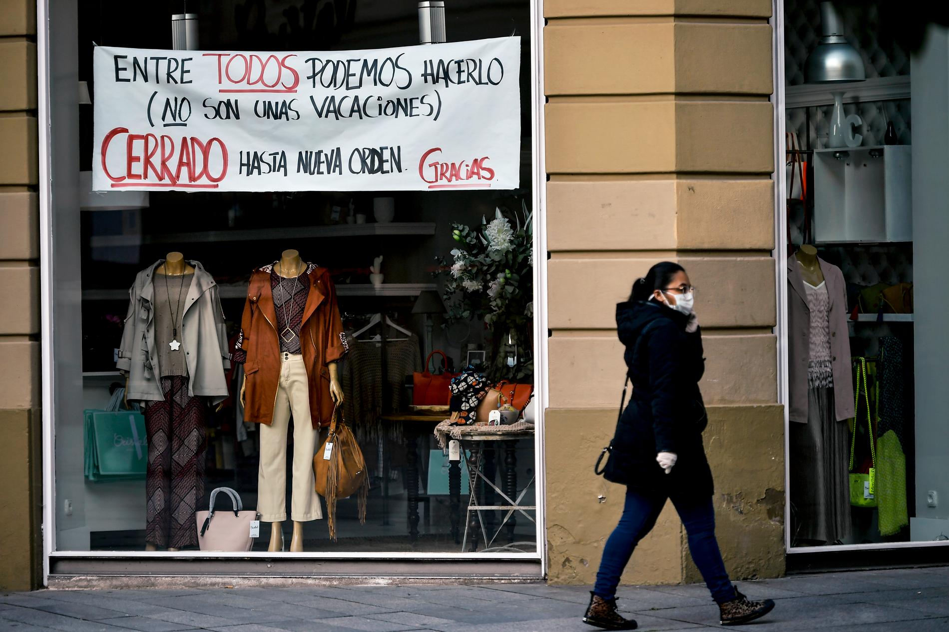 En kvinna med skyddsmask vid en stängd butik i spanska Pamplona.