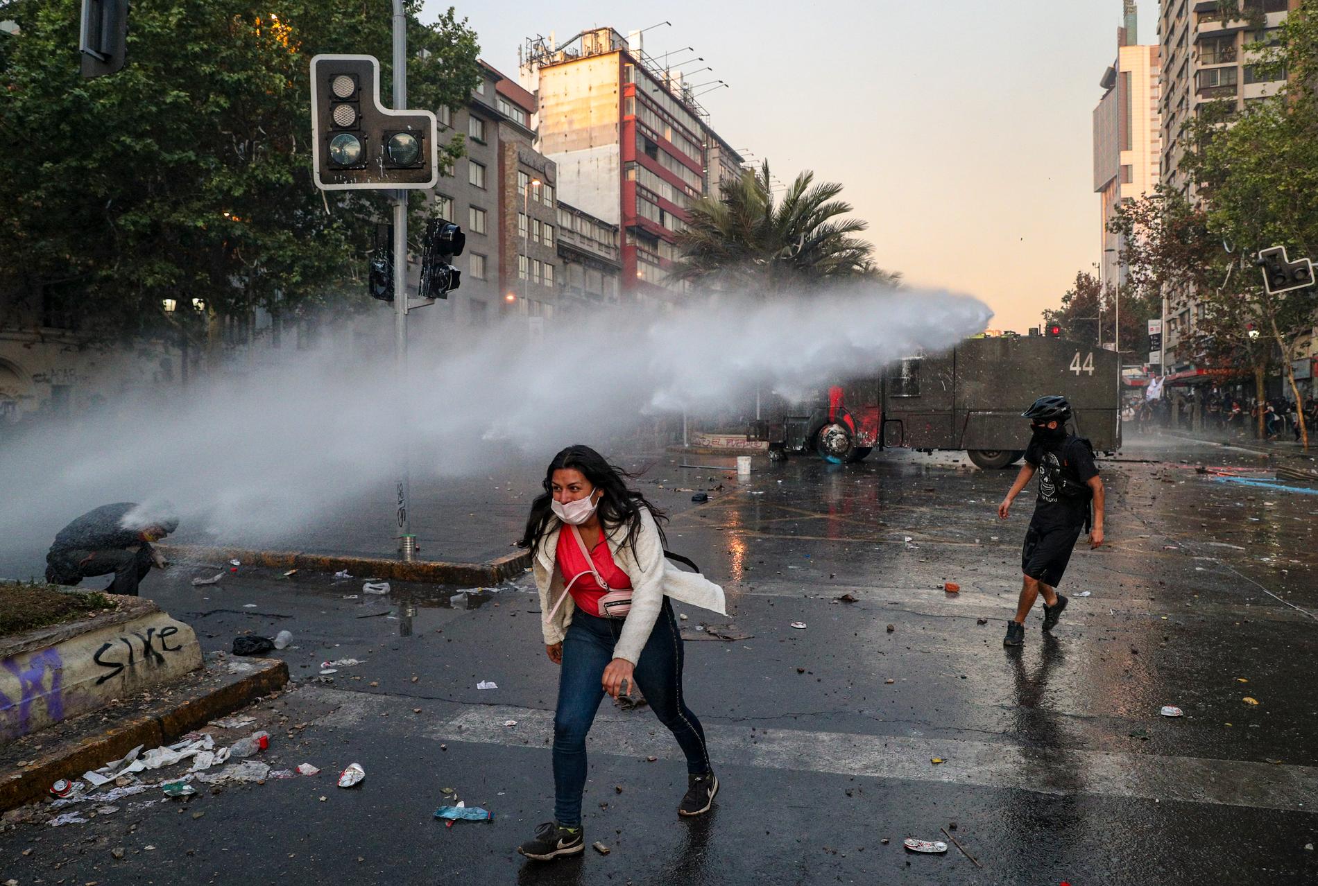 En regeringskritisk demonstrant tar sig bort från polisens vattenkanon i Santiago, Chile.