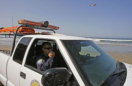 Poliser bevakar stranden där hajen slog till. I bakgrunden helikopterspaning efter hajen.