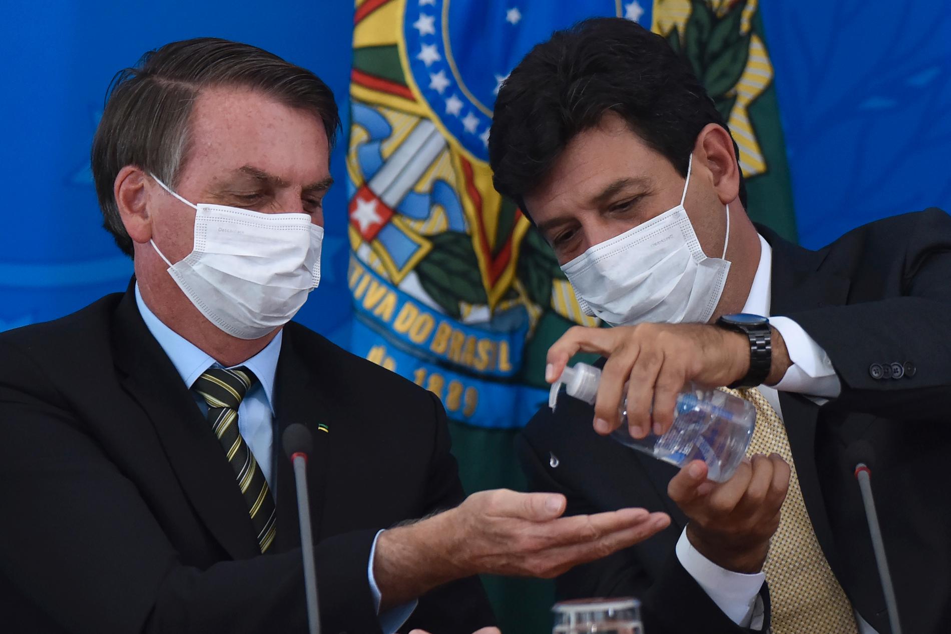 Brasiliens hälsominister Luiz Henrique Mandetta, till höger, trycker ut handsprit i sin chefs, president Jair Bolsonaros, händer under en presskonferens vid presidentpalatset i Brasilia den 18 mars.