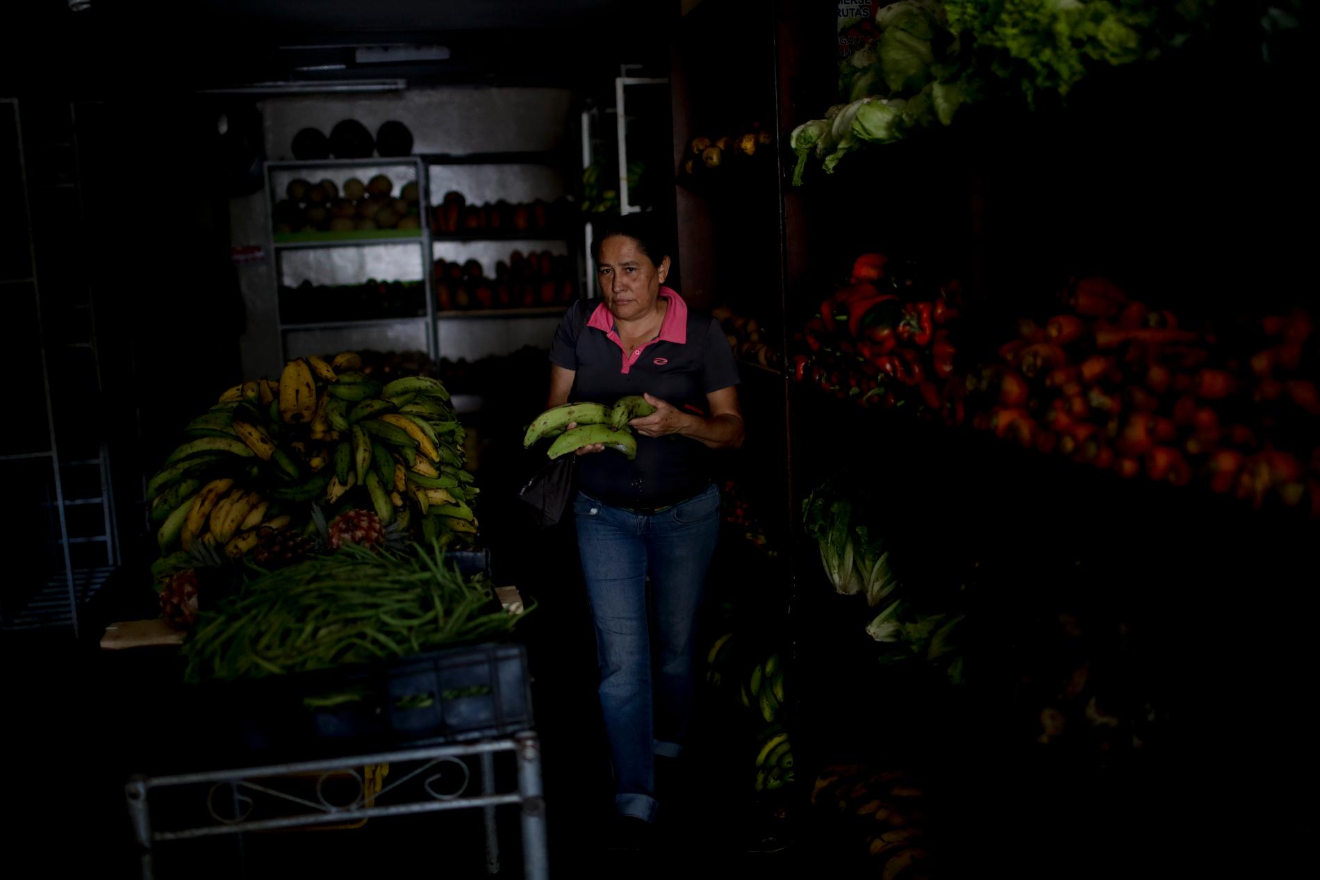 En kvinna handlar frukt i en mörklagd butik i Caracas.