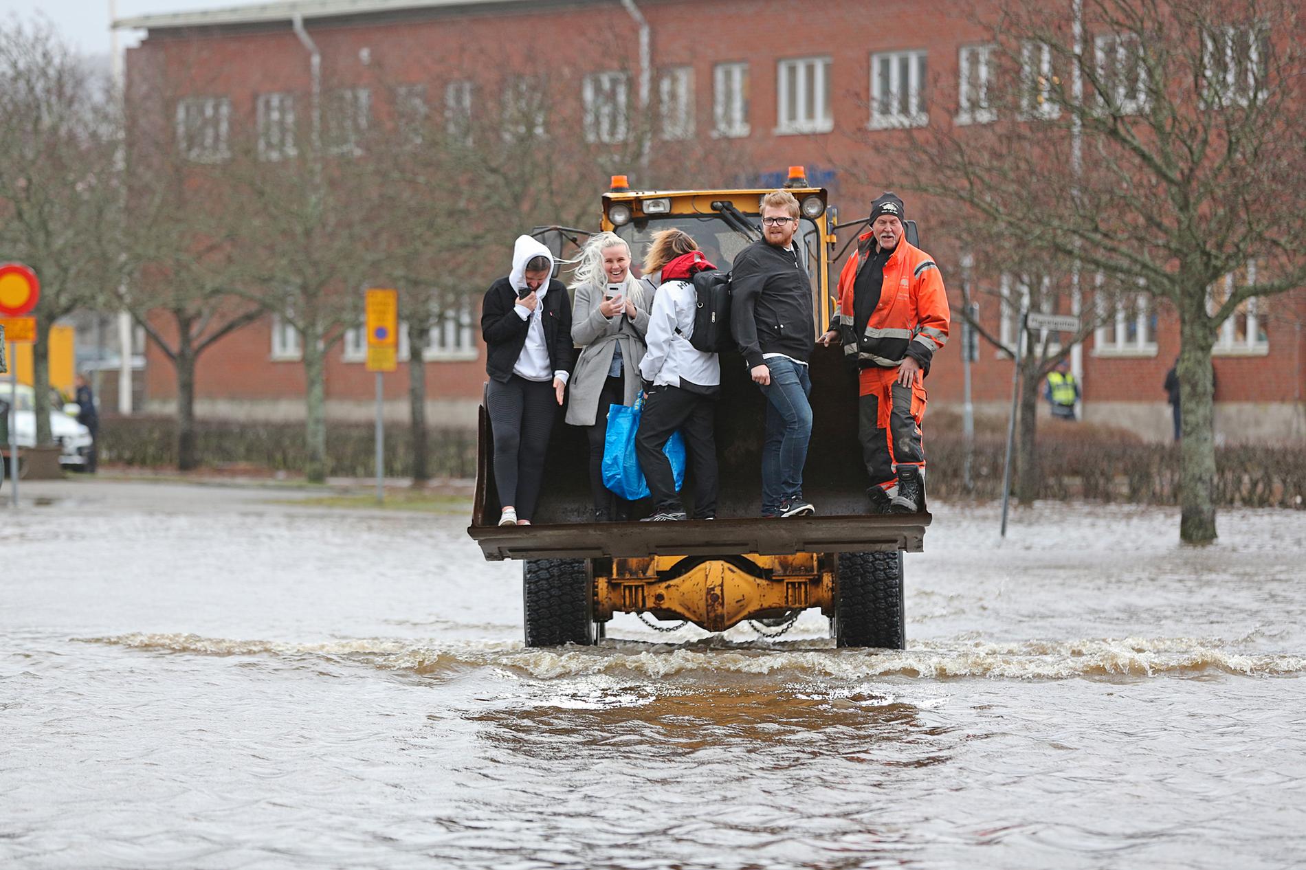 Personer får hjälp av en hjullastare att ta sig genom vattenmassorna. 