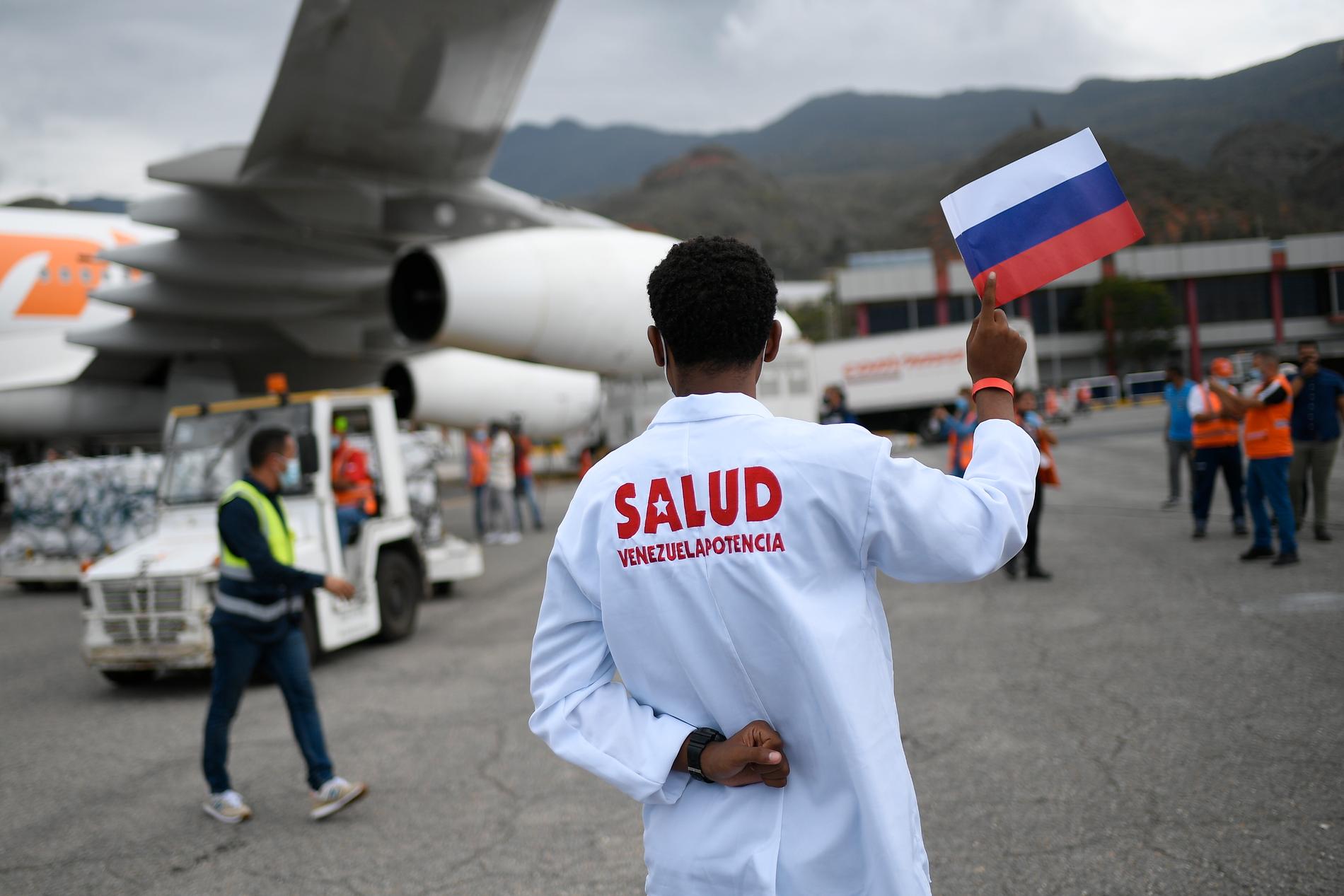 En vårdarbetare håller upp den ryska flaggan medan Sputnik V lastas av ett flygplan i Venezuela – som är ett av de länder som tar emot Rysslands vaccin. Arkivbild.