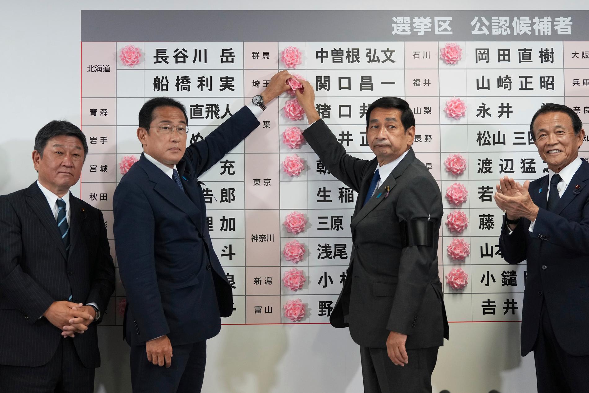 Fumio Kishida, tvåa från vänster, placerar en pappersros vid en av sina partikamraters namn, när det står klart att denna vunnit sitt val.