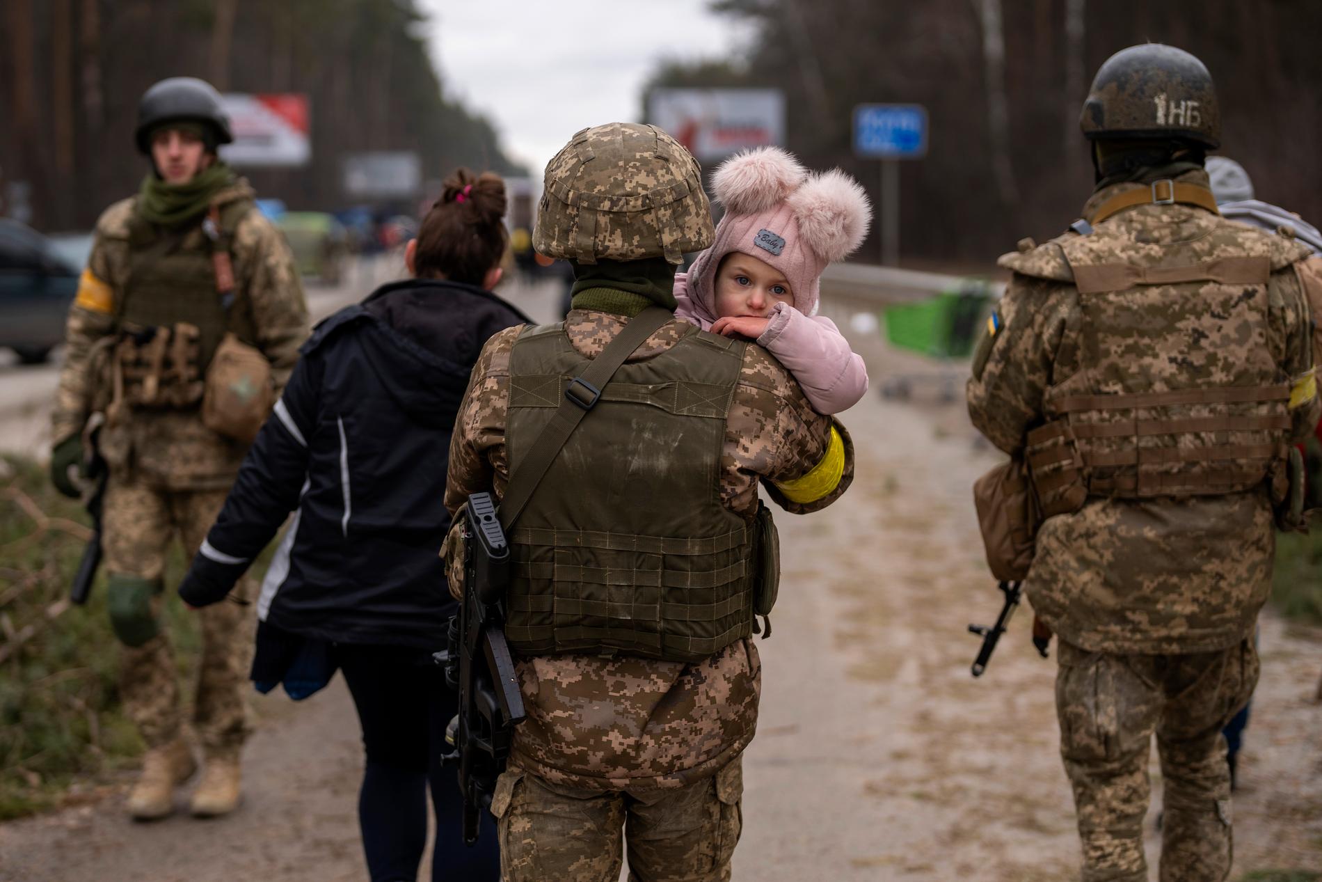 En ukrainsk soldat bär på ett barn som han hjälper att fly från Irpin, Kiev.