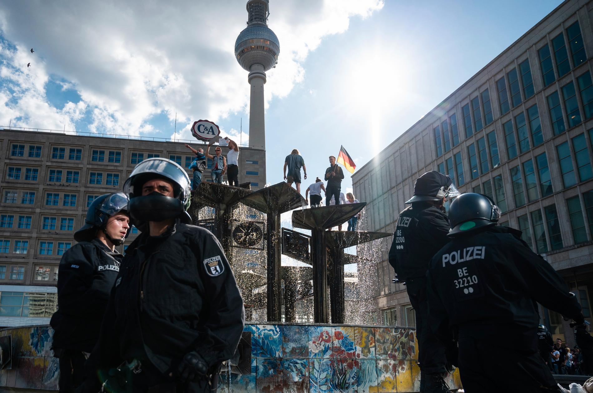 En brokig skara demonstranter protesterar mot coronarestriktioner uppe i en fontän på Alexanderplatz i Berlin.