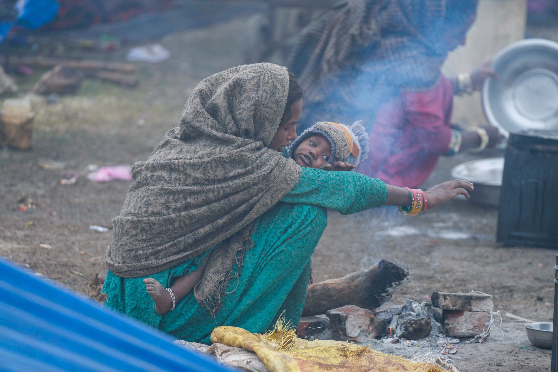 En mamma och ett barn värmer sig vid en öppen eld i Jammu.
