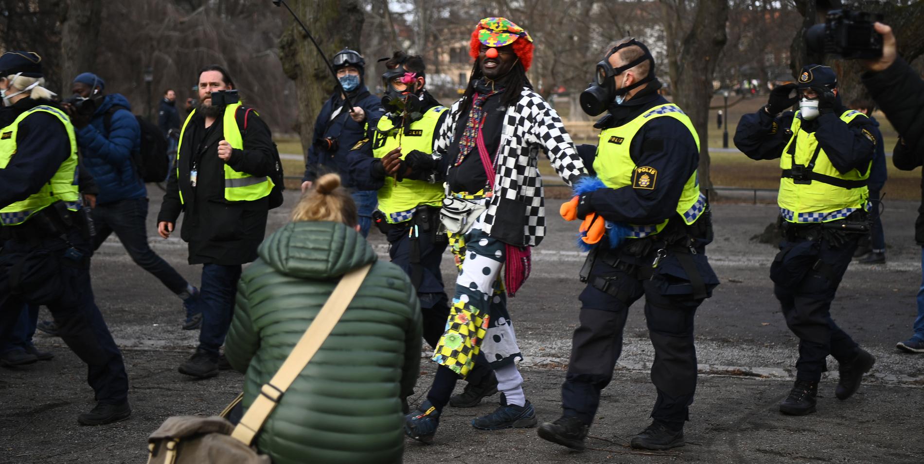 En man i lekfulla clownkläder förs bort från Humlegården i Stockholm.