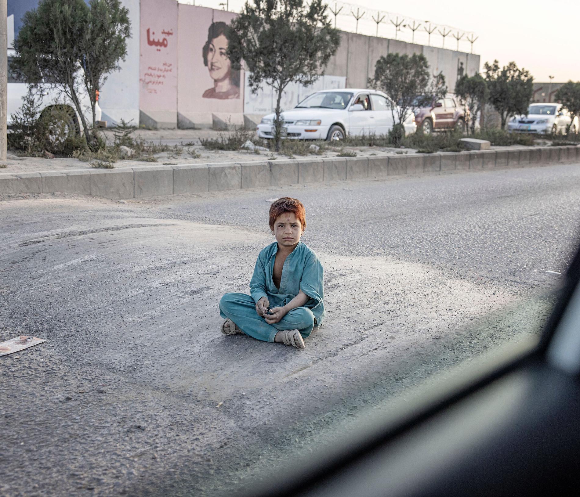 En pojke sitter mitt på gatan och tigger.