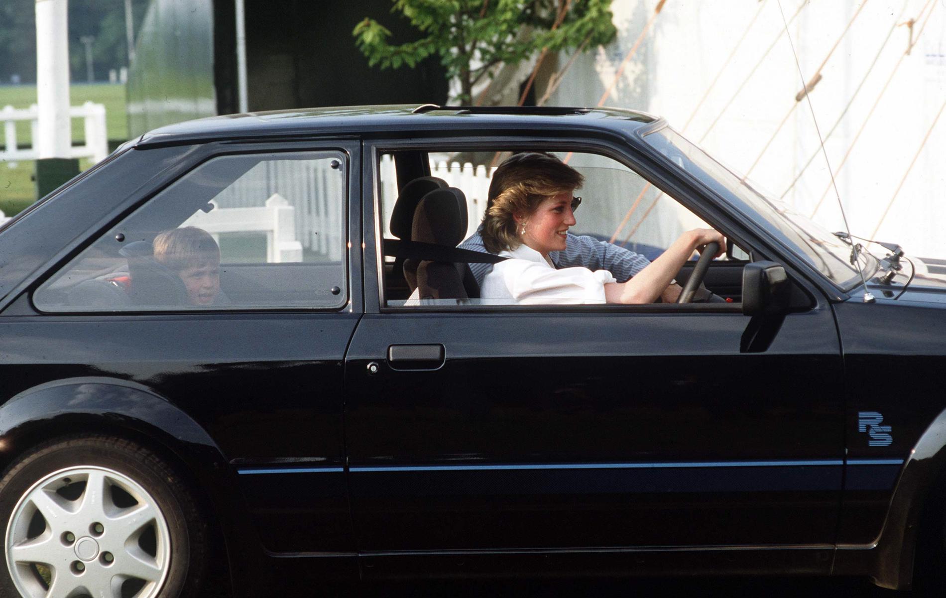 Prinsessan Diana bakom ratten med prins William i bilbarnstol i baksätet. Skymd är en livvakt från hovets personskyddsenhet, SO14, som alltid åkte med.