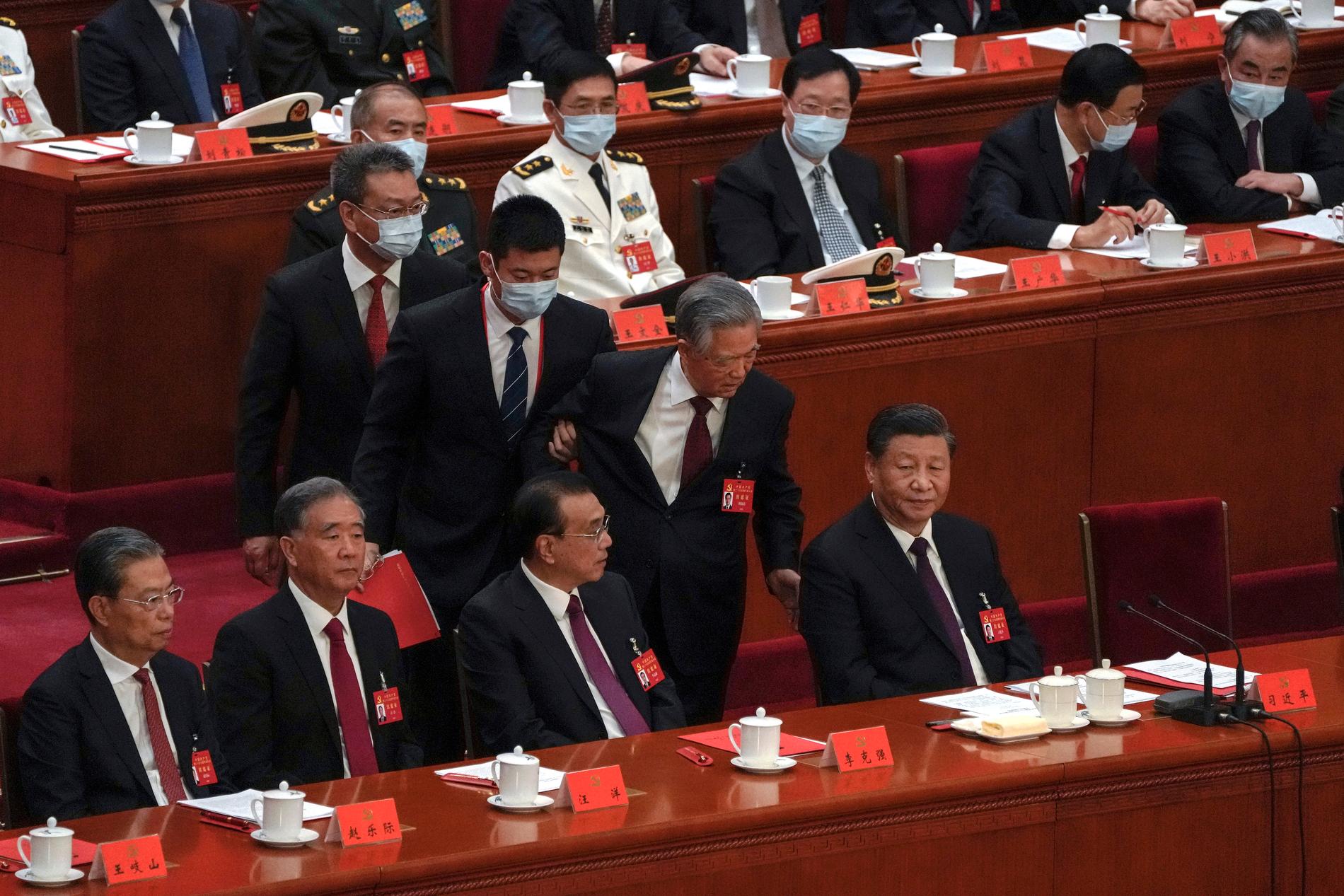 Hu Jintao, Kinas president mellan 2003 och 2013, förs bort från Folkets stora sal i Peking under partikongressens avslutningsceremoni. President Xi Jinping sitter längst till höger.