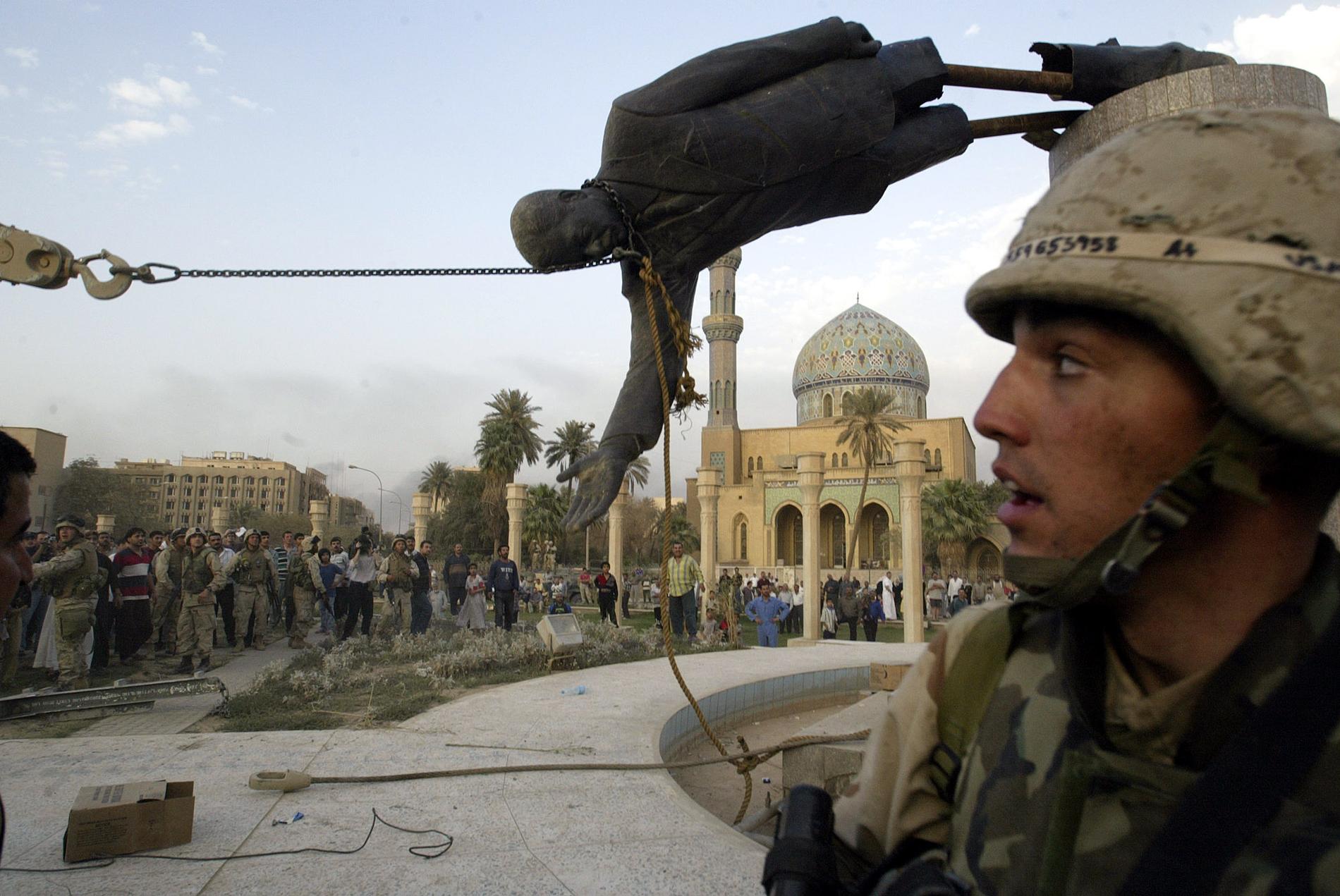 April 2003 Irakiska civila och amerikanska soldater jublar när ett pansarfordon drar ner en staty föreställande Iraks diktator Saddam Hussein.
