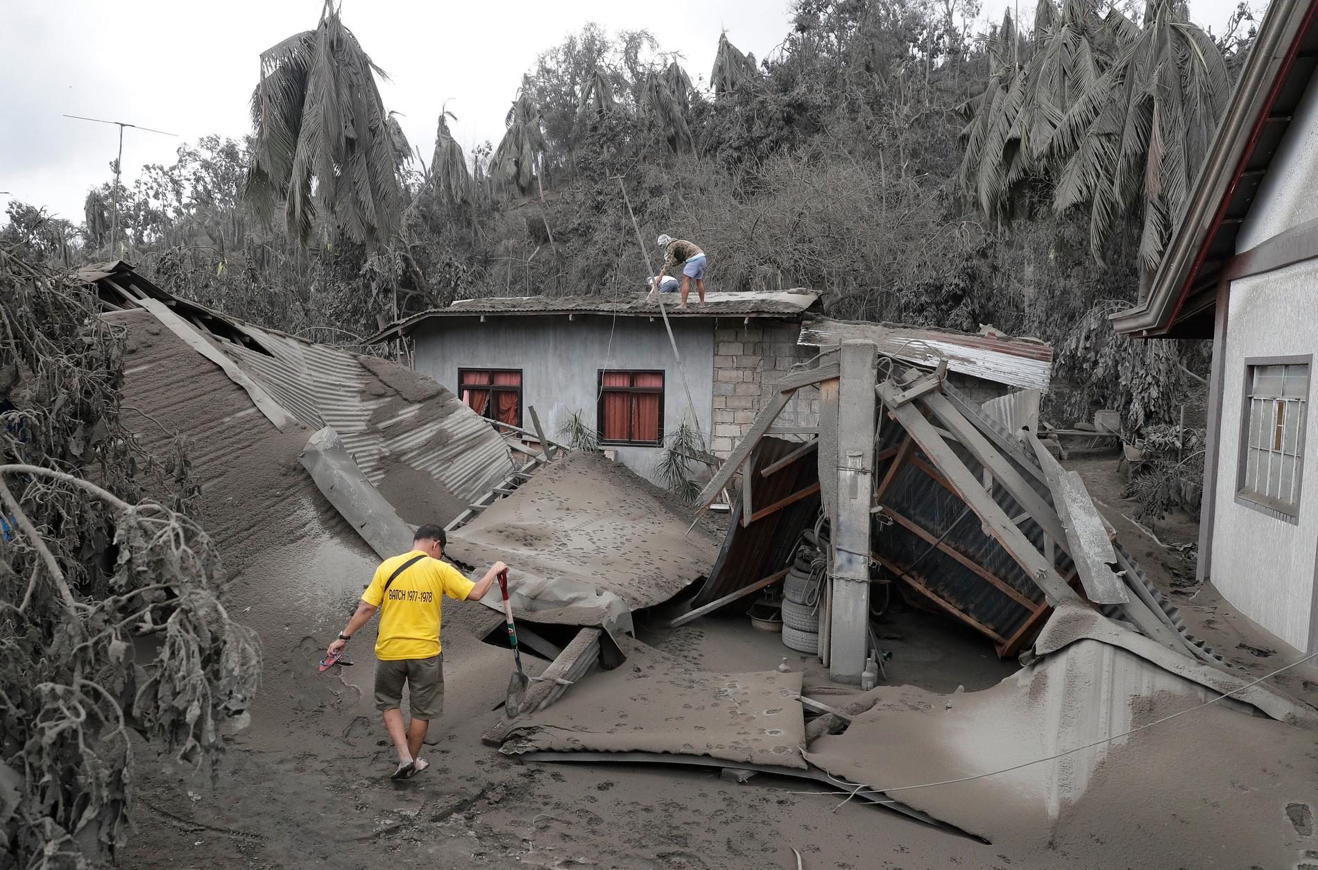 Invånare vid ett hus som förstörts av vulkanaska i södra Filippinerna.