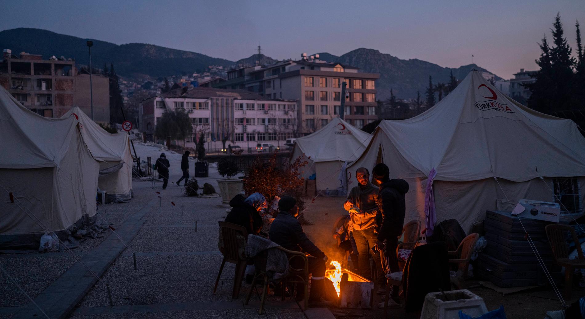 Människor samlas runt en brasa i ett tillfälligt läger i Antakya. Tusentals är hemlösa i staden efter den massiva jordbävningen i början av februari. 