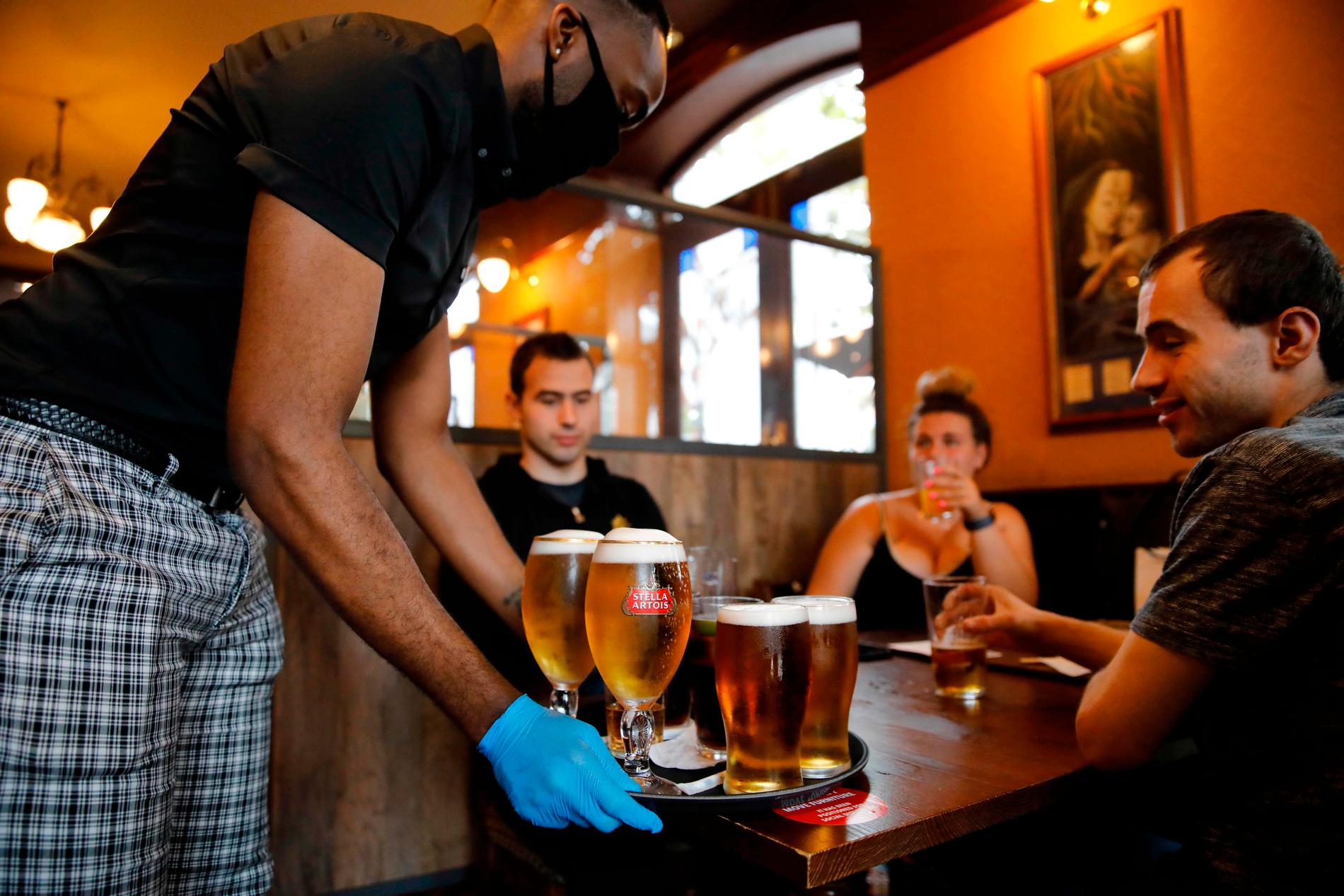 En servitör med skyddshandskar och munskydd serverar öl på lördagen till förväntansfulla gäster på en pub i Stratford i östra London.