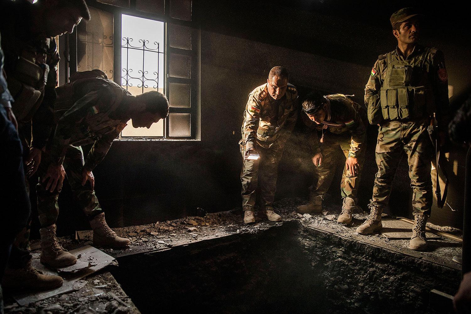 Kurdiska soldater kollar ner i en tunnel som hittades i ett av husen.