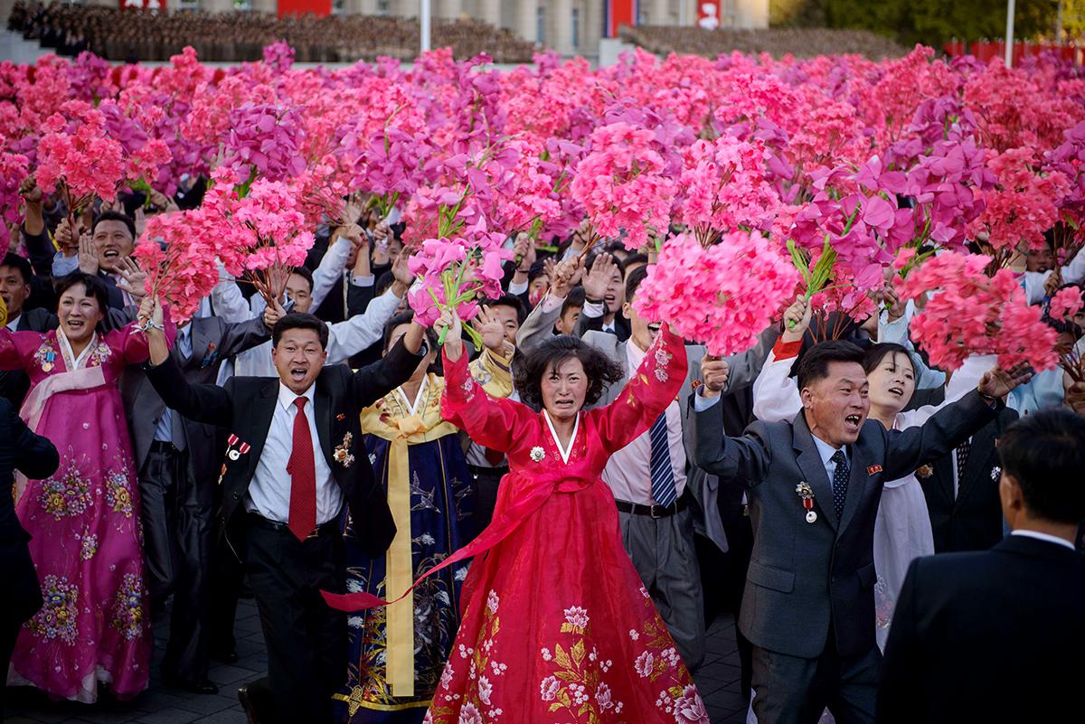 Finklädda nordkoreaner viftar med blommor under Kim Jong-Uns tal.